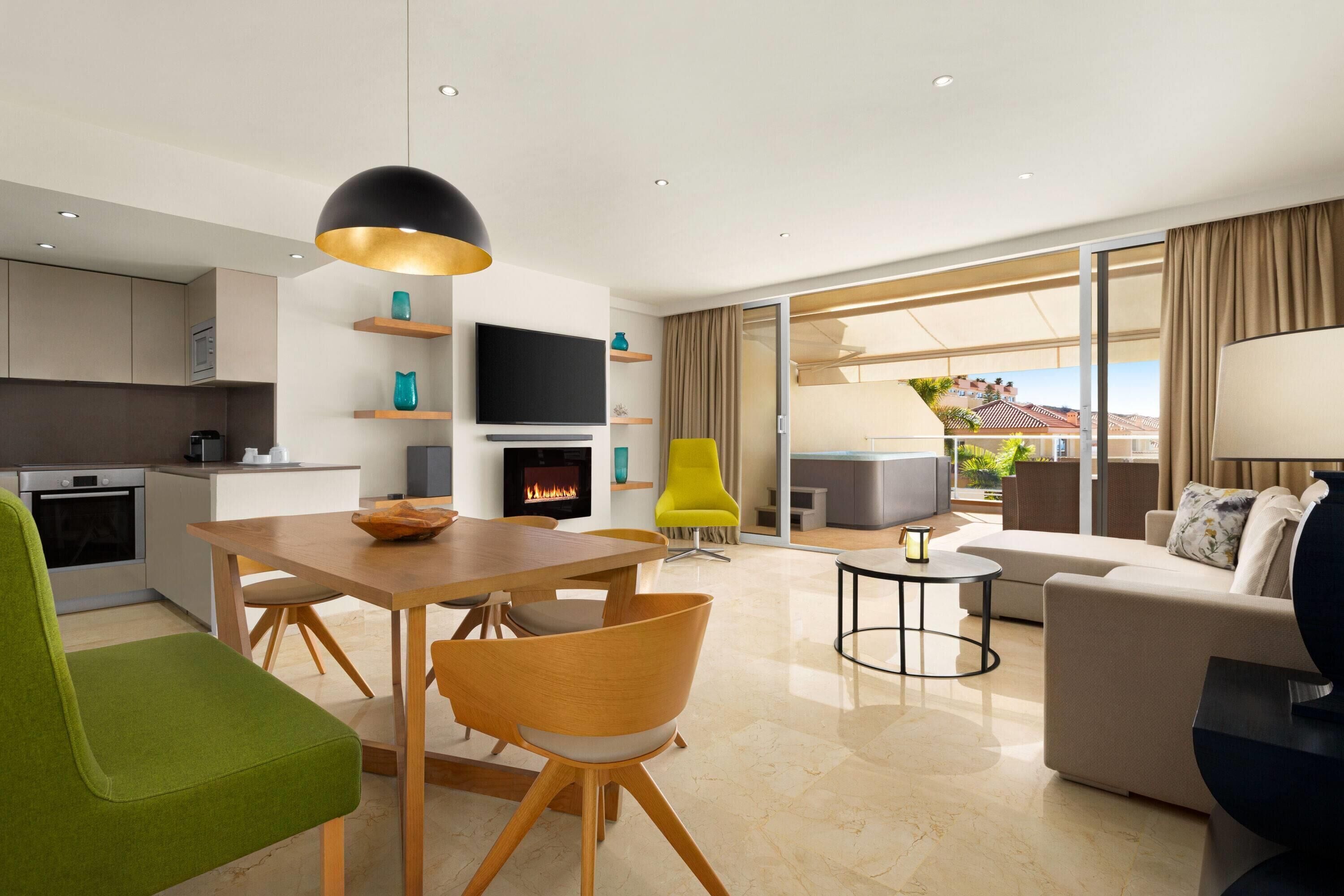 A modern living room with a dining area, a flat-screen TV, a fireplace, and a balcony with a view.