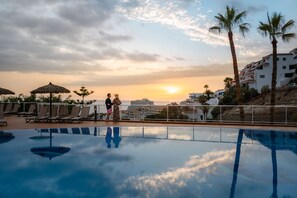 A swimming pool with lounge chairs and umbrellas, palm trees, and a sunset view. - Wyndham Residences Costa Adeje (Adeje)