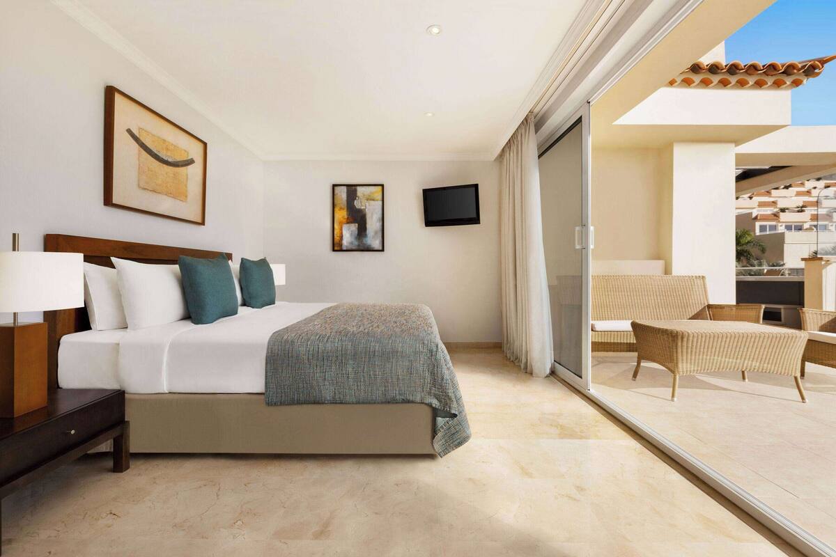 A hotel room with a bed, a desk, a chair, a TV, and a balcony with a view.