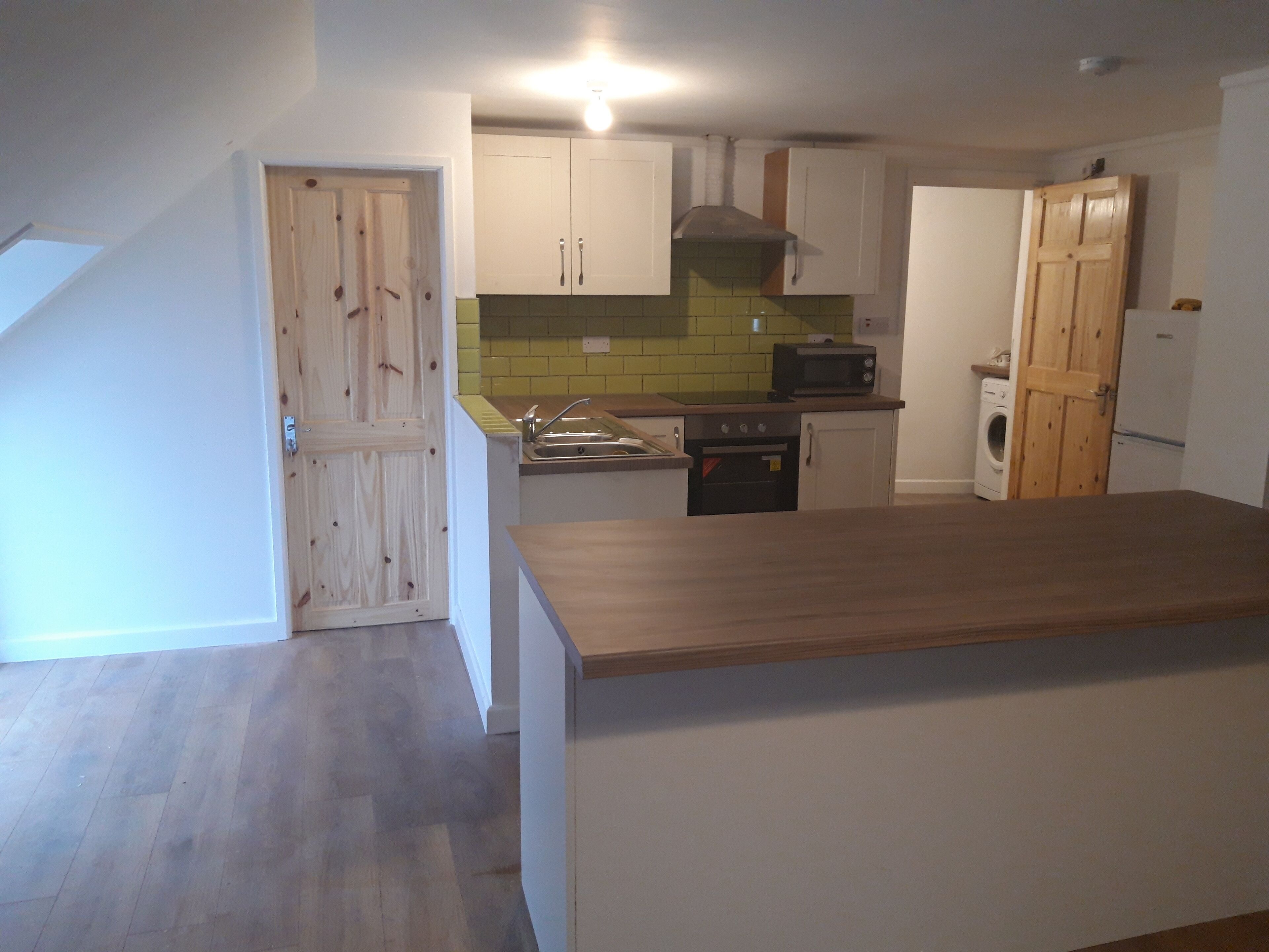 Een keuken met houten kastjes, een magnetron, een fornuis en een wasmachine.