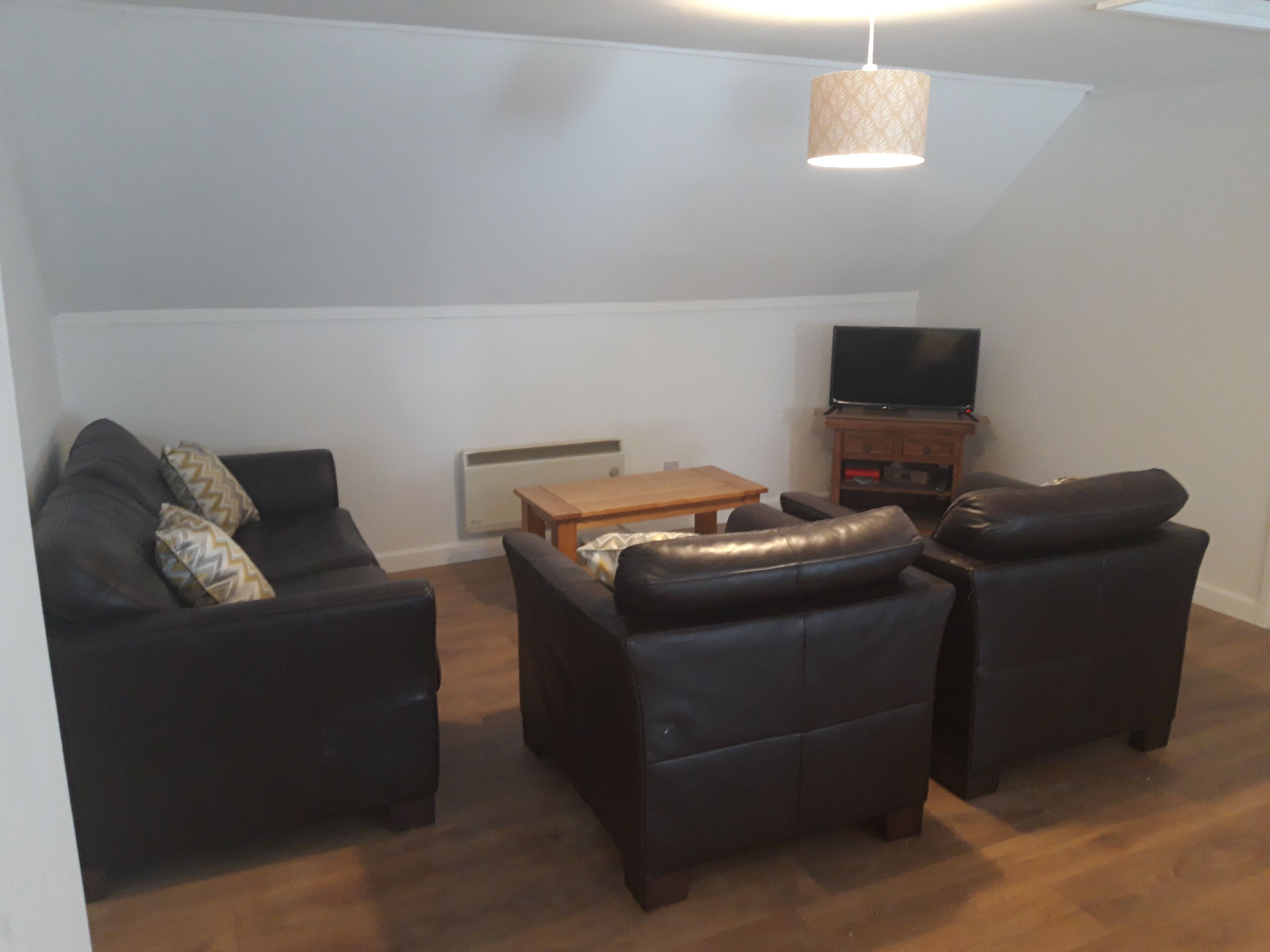 A living room with a sofa set, a coffee table, a television, and a pendant light.