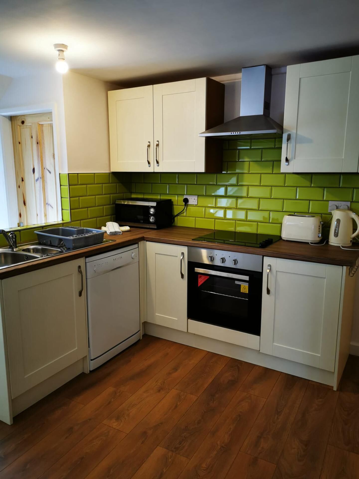 A kitchen with white cabinets, a stove, an oven, a microwave, and a green tiled backsplash.