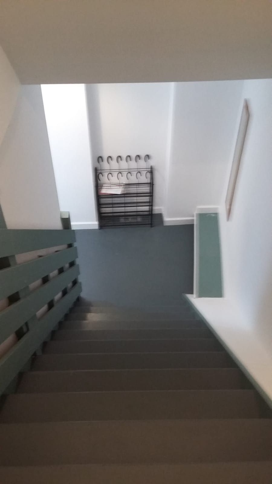 Una escala que condueix a un badiu amb una prestatgeria de metall i un quadre encarregat a la paret.