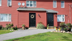 A red house with two black doors, a front porch, and satellite dishes on the roof.