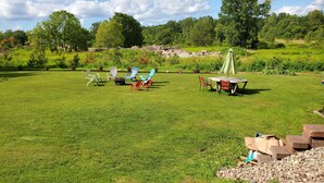 A grassy outdoor area with several Adirondack chairs, a picnic table, and a small shed.
