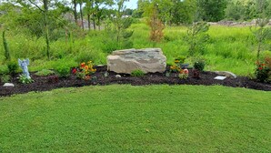 A landscaped garden with a statue, a large rock, and various colorful flowers.