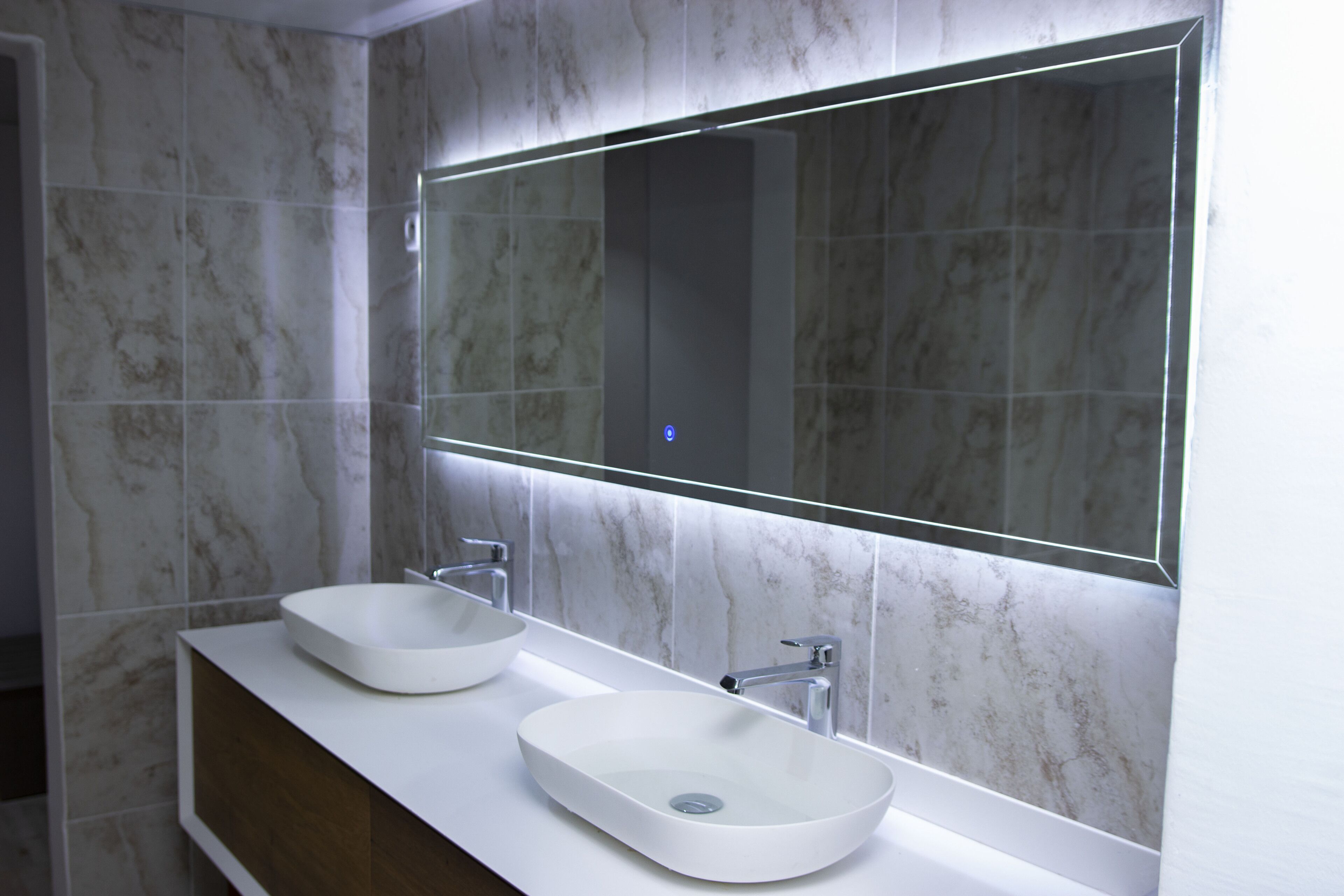 Un baño moderno con dos lavamanos blancos tipo sobremesa y un espejo grande.