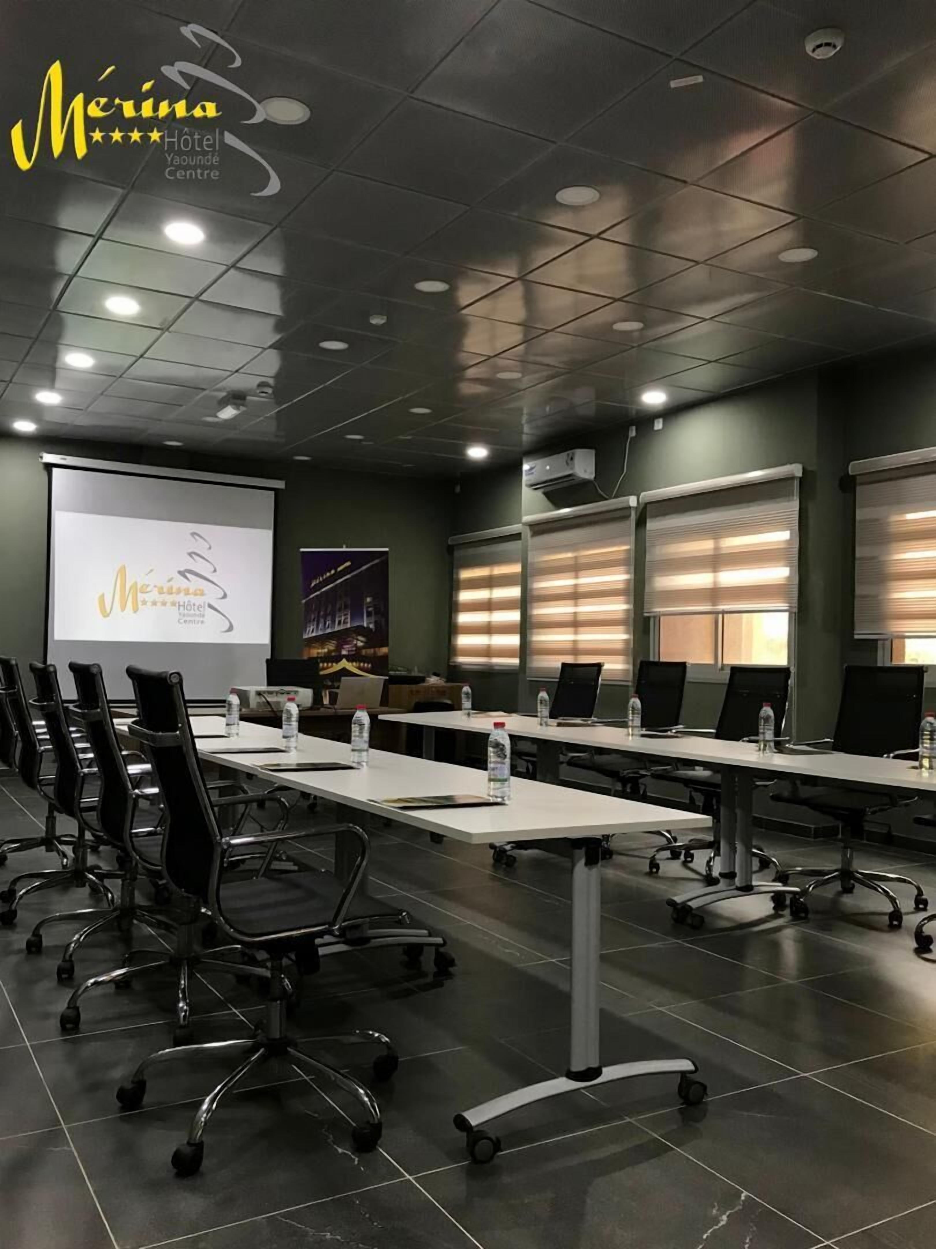 A conference room with a long table, black chairs, and a projector screen.