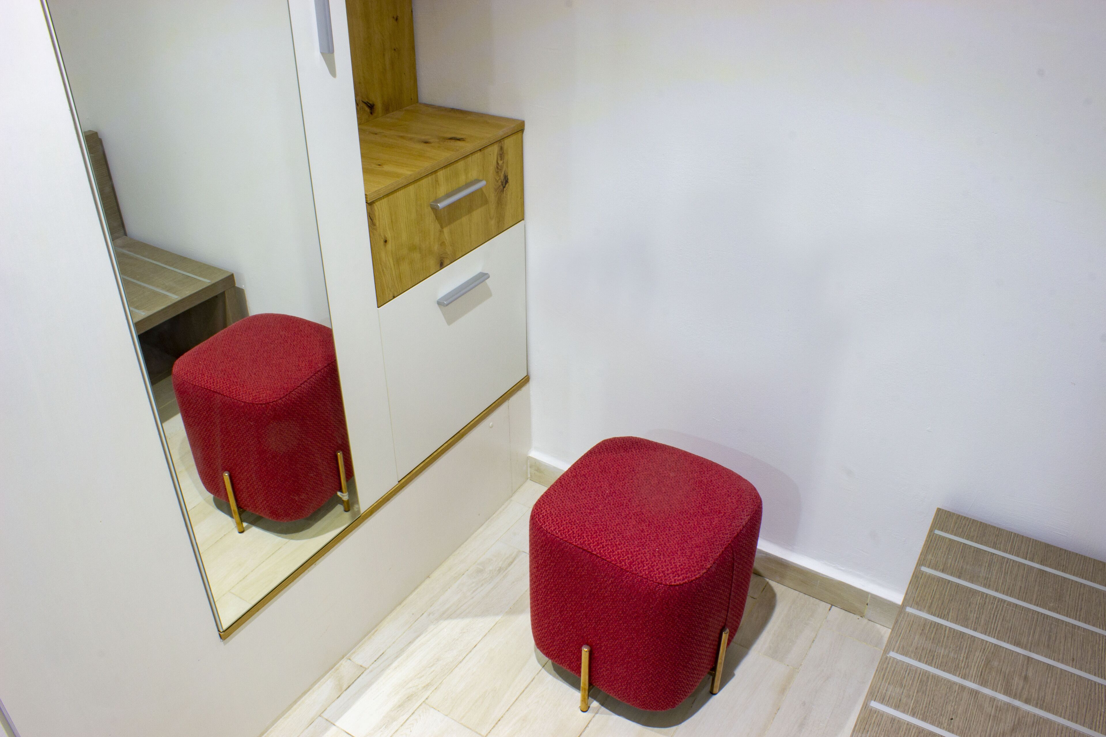 Una habitación pequeña y acogedora con un armario de madera, un espejo y un taburete rojo.