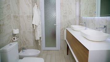 Une salle de bain moderne comprenant des toilettes, un bidet, deux lavabos et un espace douche.