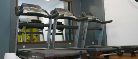 Un gimnasio con cintas de correr, un espejo y suelo de madera.