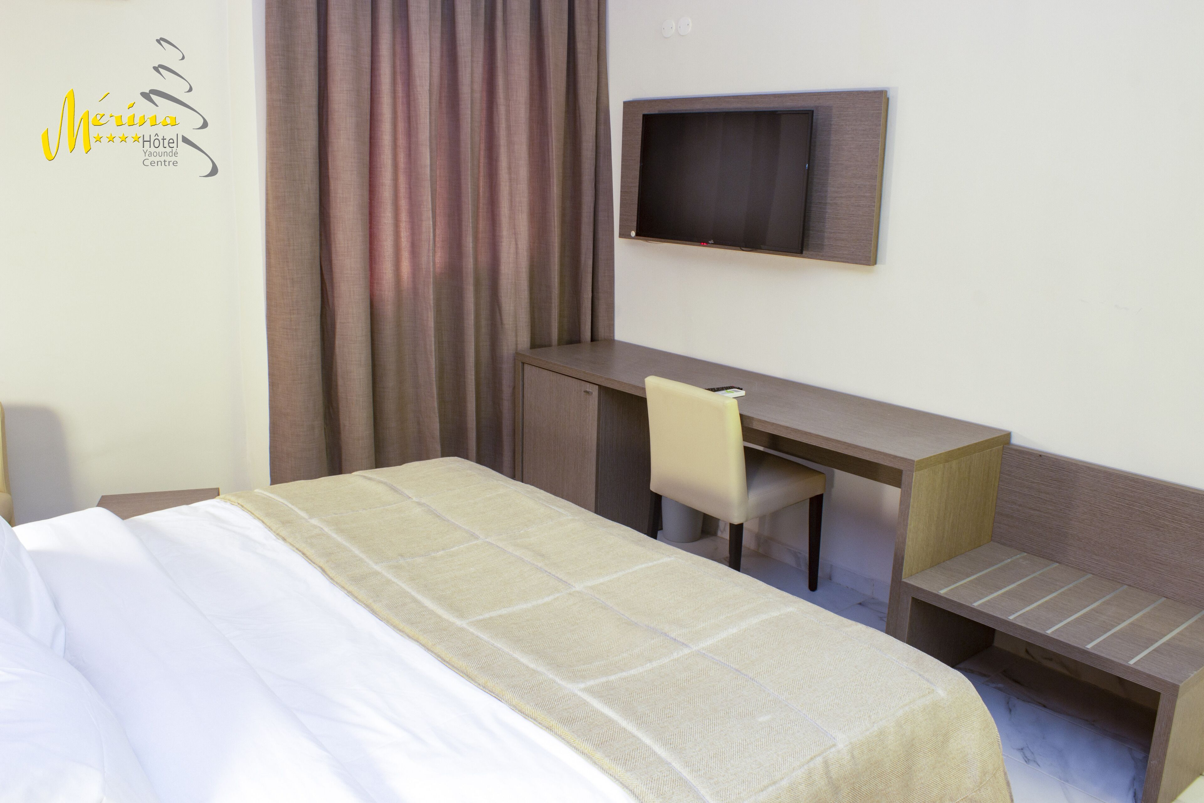 Una habitación de hotel con una cama, un escritorio, una silla y un televisor montado en la pared.