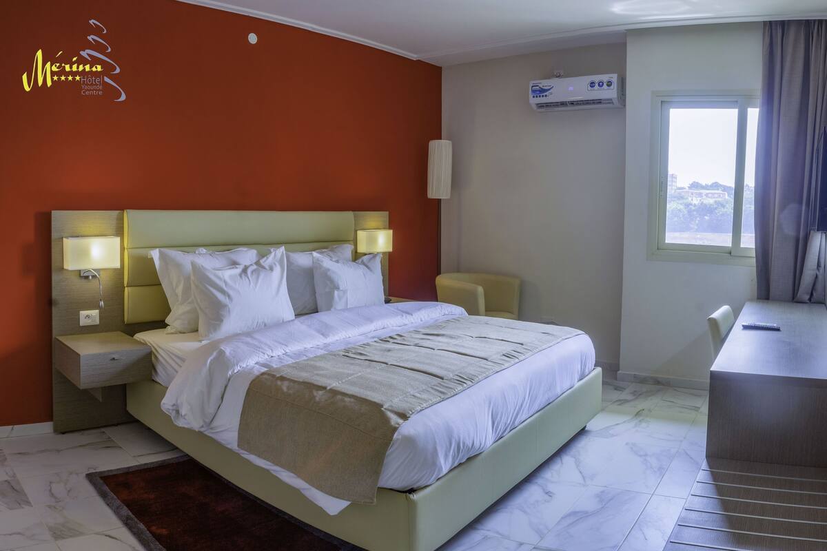A hotel room with a bed, bedside lamps, a desk, and a window.