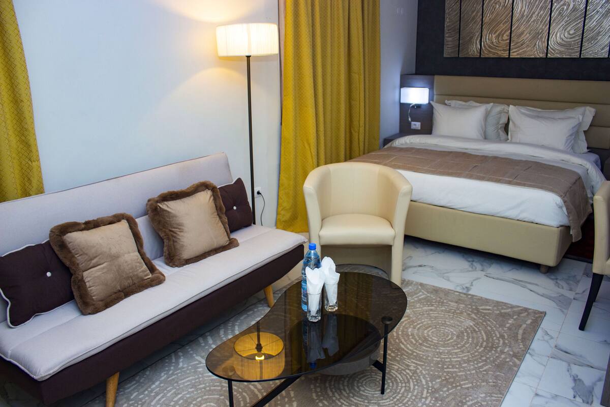 A hotel room with a bed, a sofa, a chair, a coffee table, and a lamp.