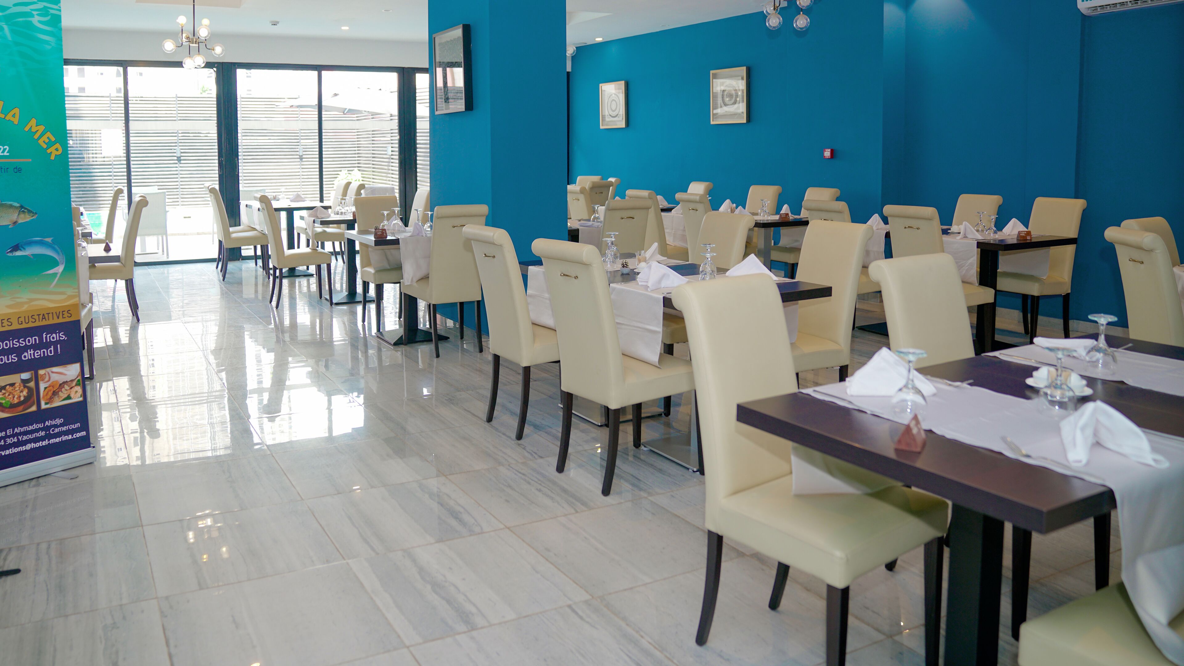 A restaurant with multiple tables and chairs, a blue wall, and a large poster on the left.