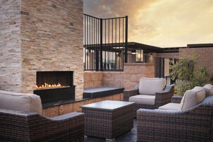An outdoor patio area with a stone wall, a black fire pit, wicker furniture, and a view of the sky.