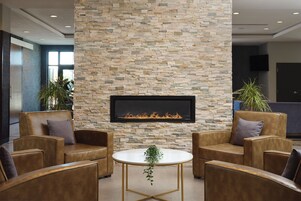 A modern lobby with leather sofas, a stone accent wall, a fireplace, and potted plants.