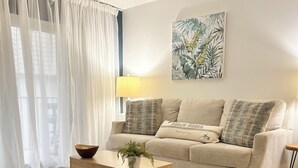 Un salon avec un canapé, une table d’appoint sur laquelle est posée une plante, une lampe et un tableau accroché au mur.