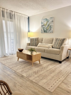 A living room with a sofa, a side table with a plant, a lamp, and a painting on the wall.