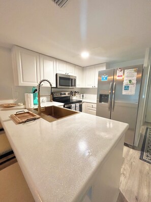 A modern kitchen with white cabinets, stainless steel appliances, and a large island with a sink. - Coquina A202: Seaside Oasis Beach front Condo (St. Augustine)