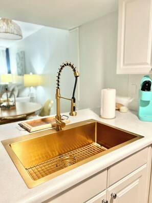 A kitchen with a gold sink, white cabinets, and a teal coffee machine. - Coquina A202: Seaside Oasis Beach front Condo (St. Augustine)