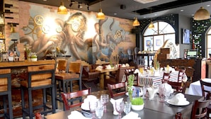 En restaurant med et mural af mekaniske tandhjul og en blæksprutte, møbler i træ og et barområde.