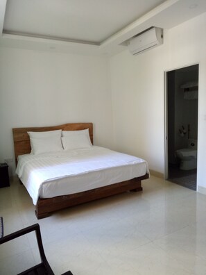 A bedroom with a wooden bed, white bedding, a nightstand, and a door leading to a bathroom.