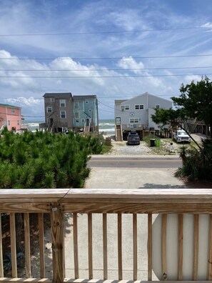A coastal residential area with a view of the ocean, featuring multi-story buildings, a sandy beach, and a wooden deck.