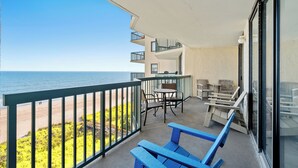 Un balcon avec vue sur la plage, des meubles d’extérieur et une rambarde.