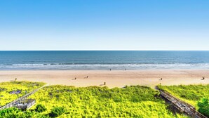 Une plage avec une promenade en bois qui mène à une zone herbeuse.