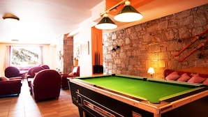 Une table de billard avec un mur en pierre en arrière-plan, des sièges rembourrés de couleur rouge et une vue sur un paysage montagneux par une fenêtre.