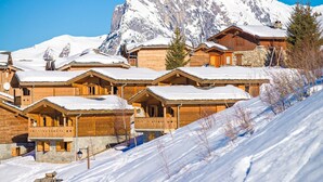 Une rangée de chalets en bois aux toits enneigés, se dressant sur fond de montagnes aux sommets couverts de neige.