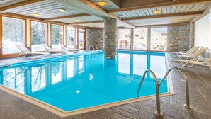 Une piscine intérieure à l’eau d’un bleu cristallin, avec des murs en pierre et des poutres en bois.