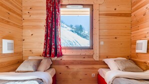 Une cabane avec deux lits, une fenêtre donnant sur un paysage enneigé et des murs en bois.