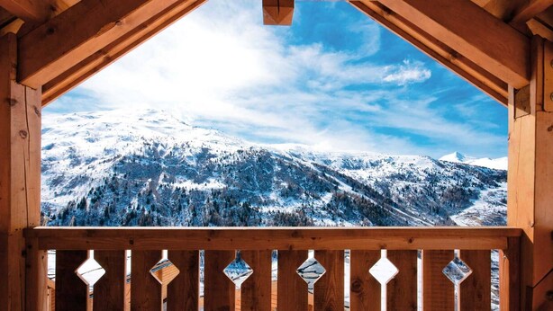 Un balcon en bois offrant une vue sur des montagnes enneigées.