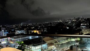 Un balcón con muebles de mimbre y vista a un paisaje urbano nocturno.