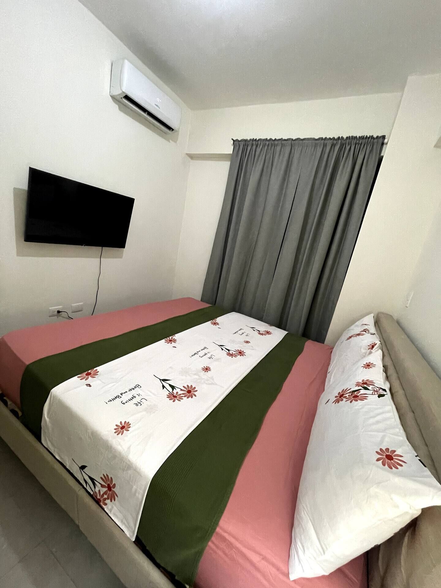 Une chambre à coucher avec un lit, un téléviseur à écran plat fixé au mur et une fenêtre avec des rideaux.