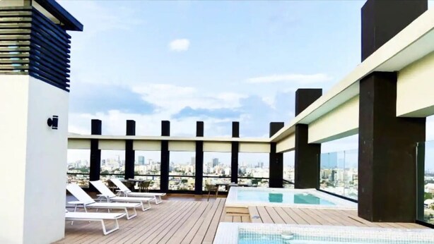 Zona de piscina en la azotea con sillones y vistas del horizonte urbano.