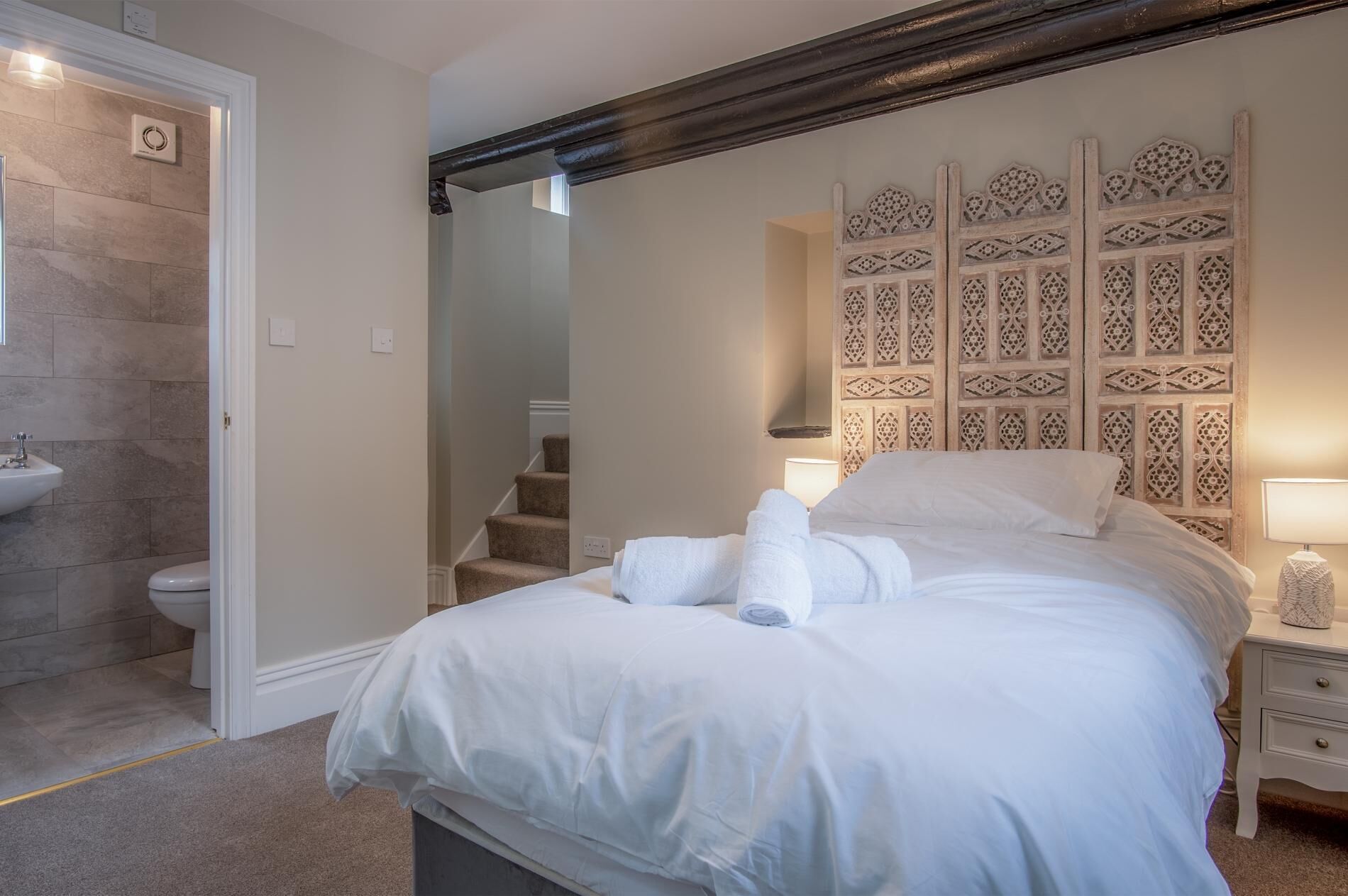 A hotel room with a bed, a nightstand, a lamp, a bathroom with a sink and toilet, and a staircase.