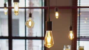 A breakfast bar with hanging light bulbs, a coffee station, and a window with blinds in the background.