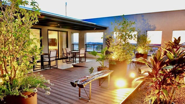 A rooftop terrace with a wooden deck, seating area, and potted plants.