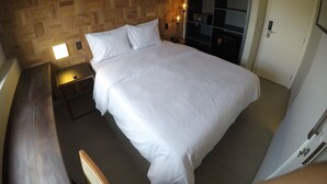 A neatly made bed with white linens, a wooden headboard, a bedside table with a lamp, and a wardrobe with a mirror.