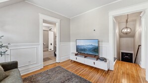 Ein Wohnzimmer mit Flachbildfernseher auf einer weißen Konsole, Holzboden und einem gemusterten Teppich.