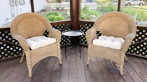 Eine überdachte Veranda mit Korbstühlen und einem kleinen Tisch, mit Blick auf eine Wohngegend mit weißen Zäunen und parkenden Autos.