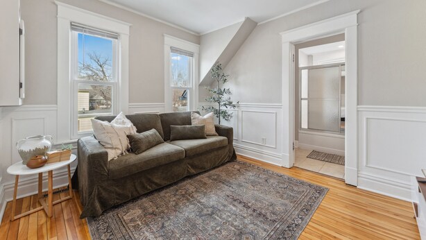 Ein Wohnzimmer mit einem braunen Sofa, einem gemusterten Teppich und einer weißen Wand mit einem Fenster.