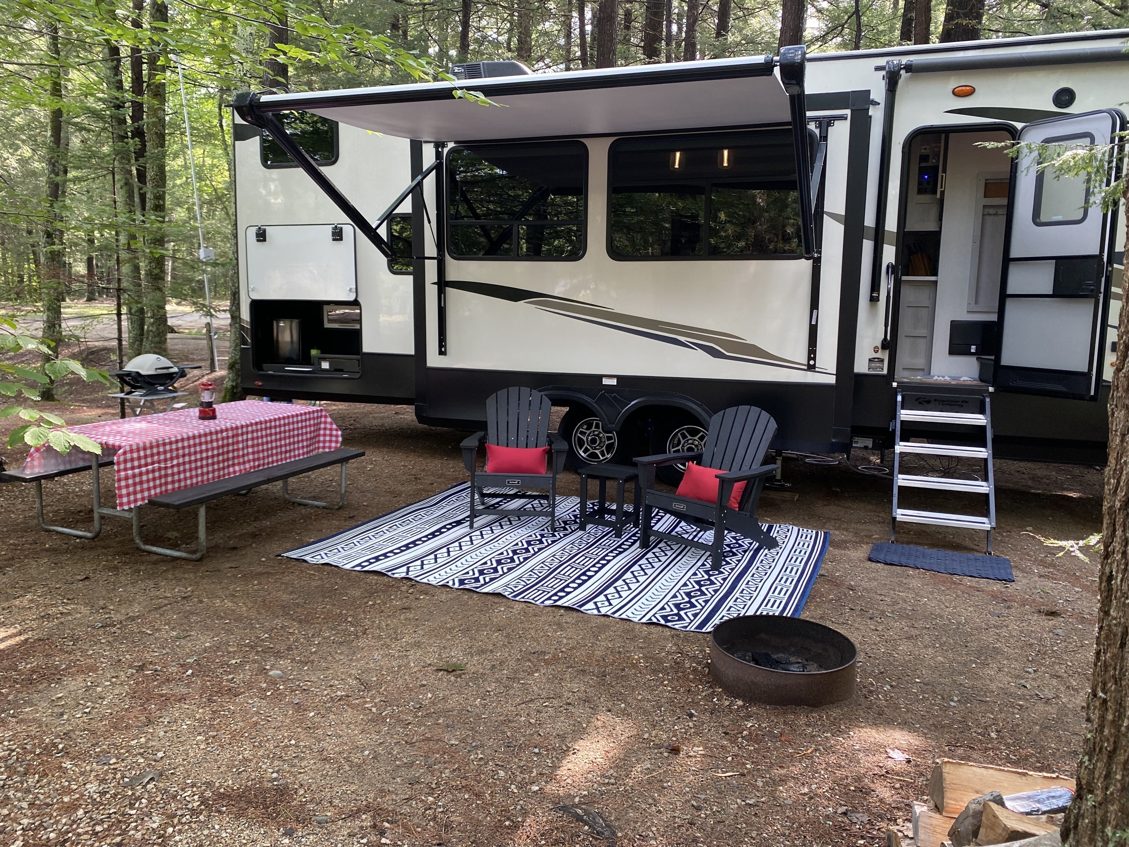 Un véhicule récréatif doté d’un espace repas couvert, de deux fauteuils Adirondack, d’une table de pique-nique et d’un barbecue.