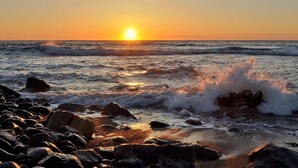 En strand med bølger der slår ind mod kysten og en solnedgang i baggrunden.