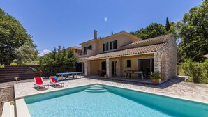 A two-story house with a swimming pool, outdoor seating, and a stone wall.