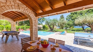 A covered outdoor area with a pool, dining table set with plates and glasses, and a pool table.