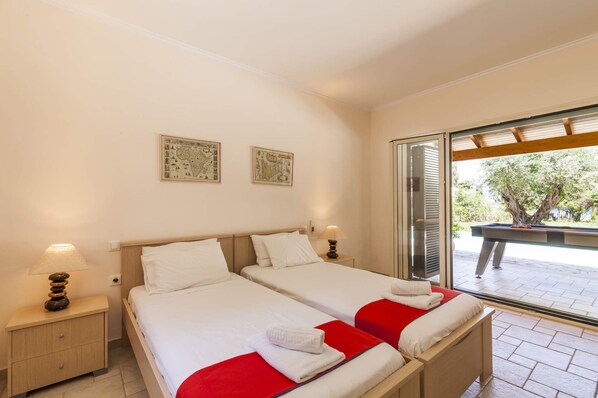 Habitación doble con dos camas, cabecera de madera, mesita de noche con lámpara y un amplio ventanal corredero que da a un área exterior.